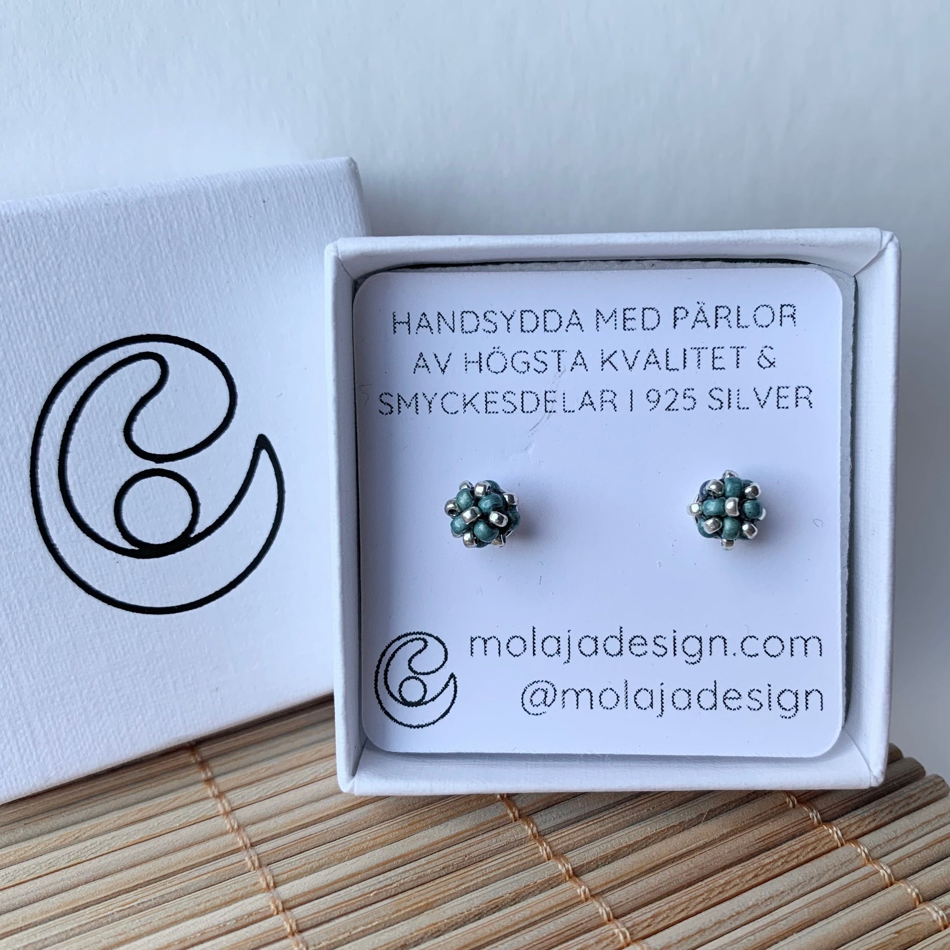 Metallic blå studs i smyckesask med text från MoLaja Design.