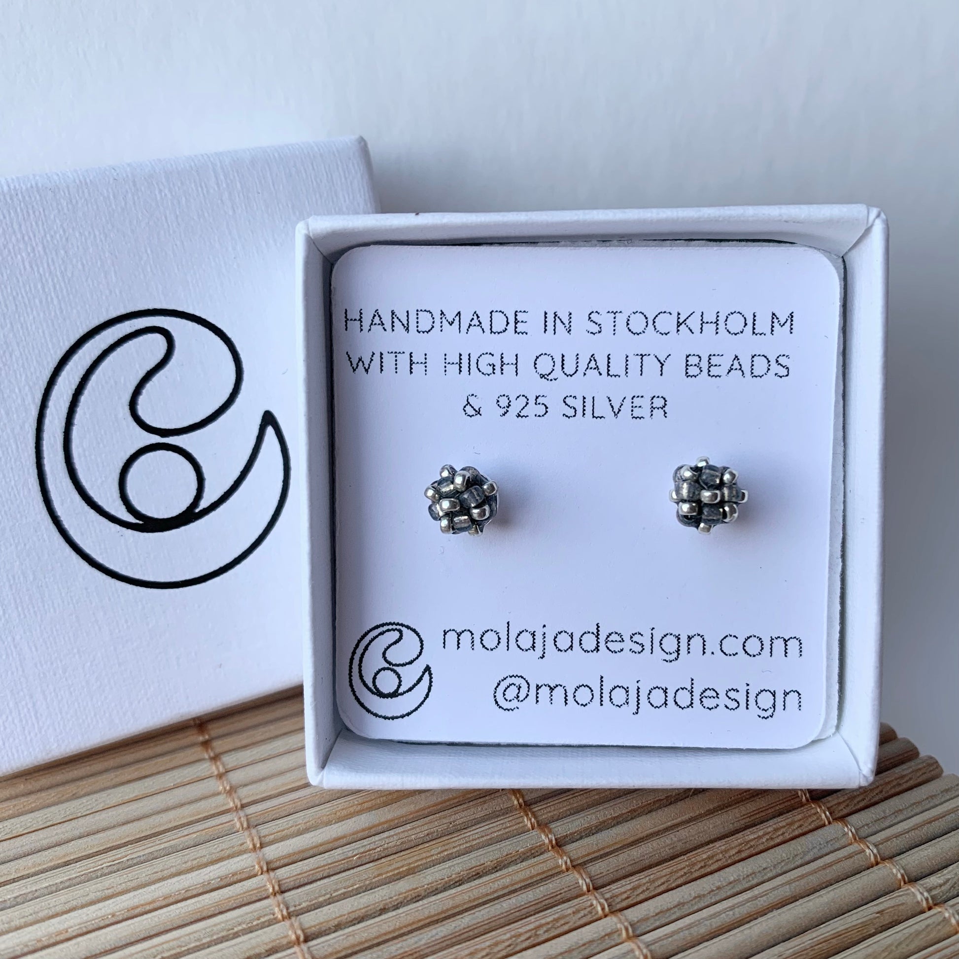 Transparent mörk grå studs i smyckesask med text från MoLaja Design.